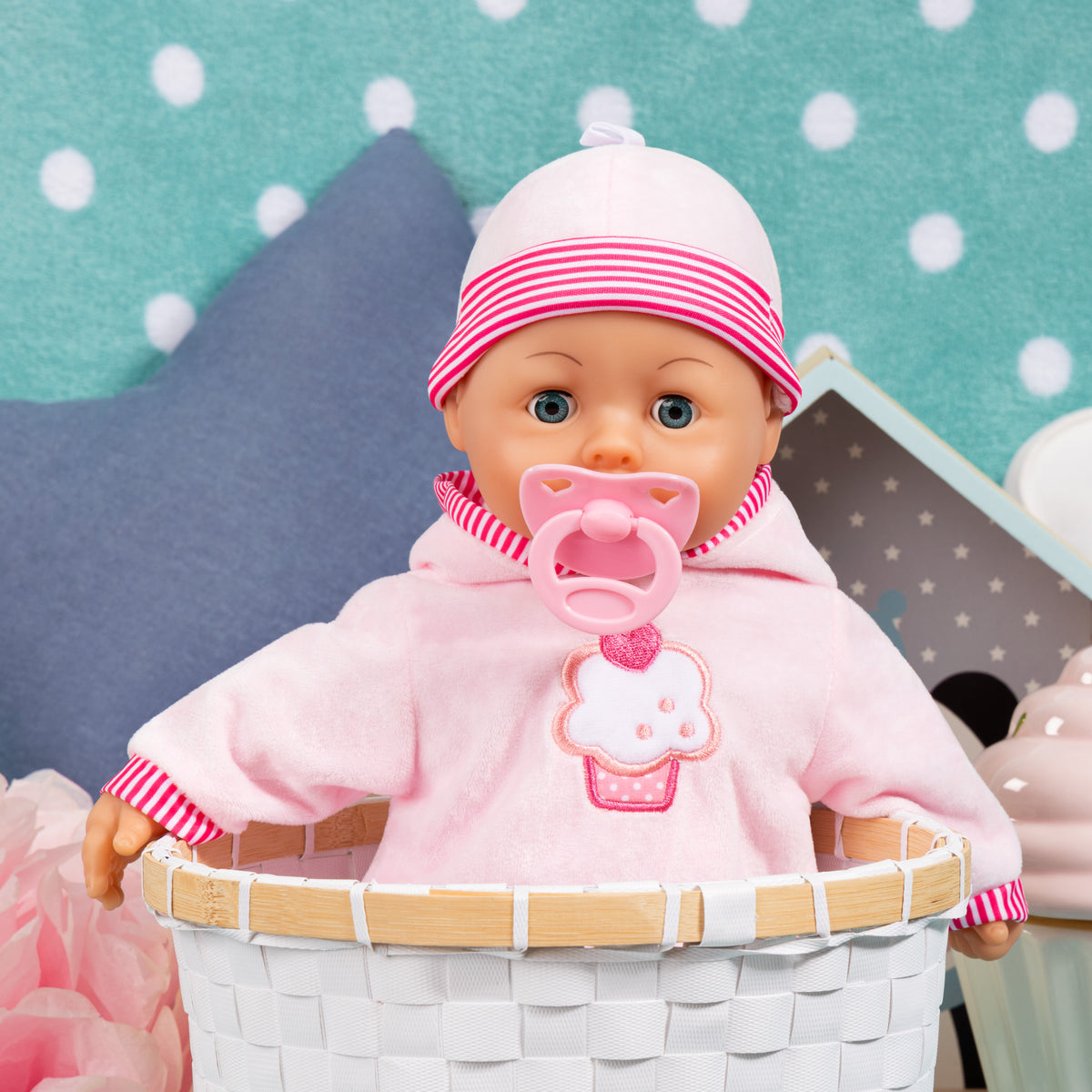 Pink baby doll wearing striped hat and pacifier, seated in white basket