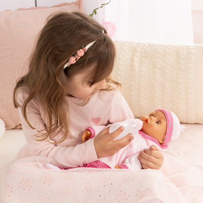 Child holding pink baby doll with striped hat and pacifier on a bed