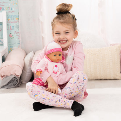 Smiling child sitting with pink baby doll in striped hat and cupcake outfit