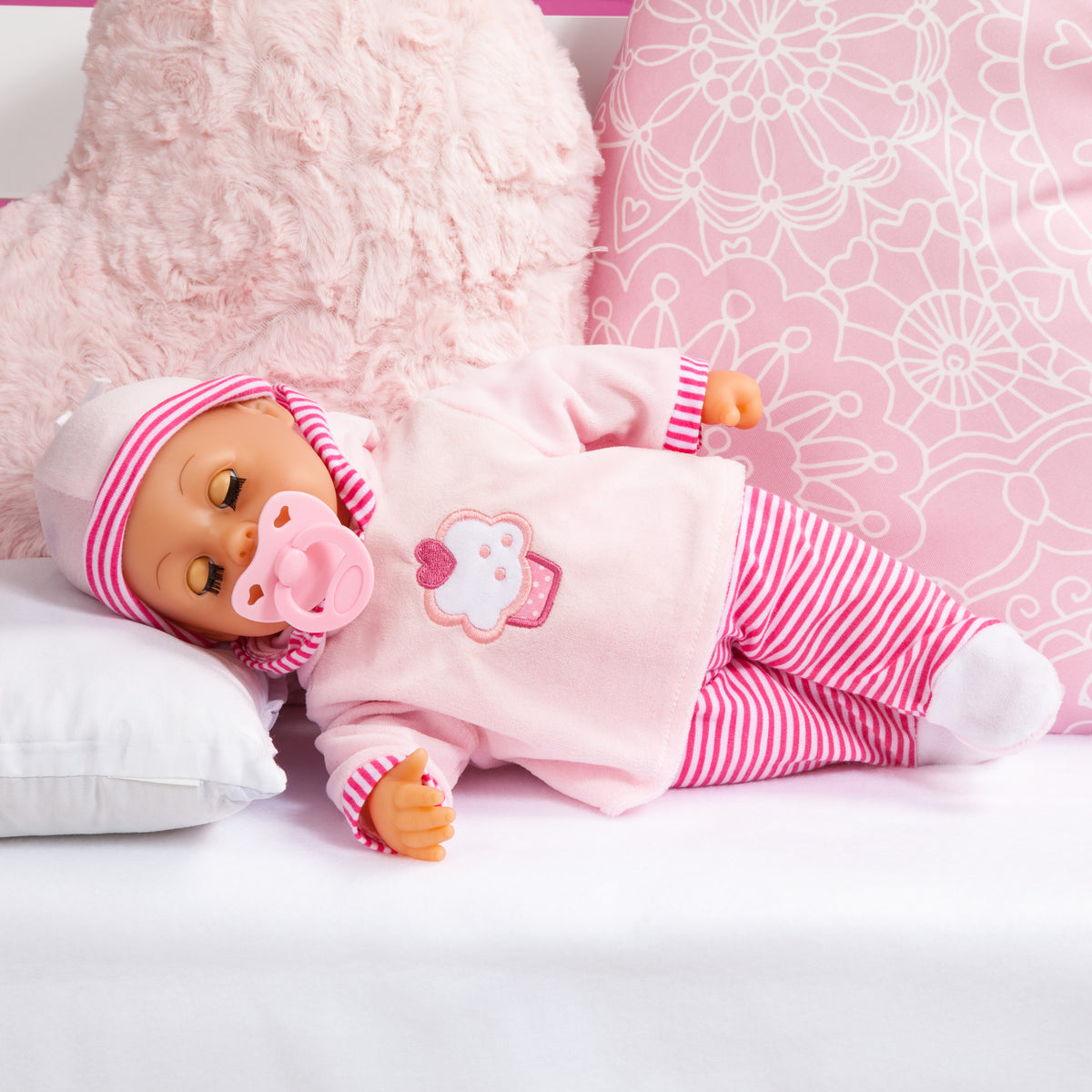 Pink baby doll lying on white bedding, striped outfit with cupcake logo