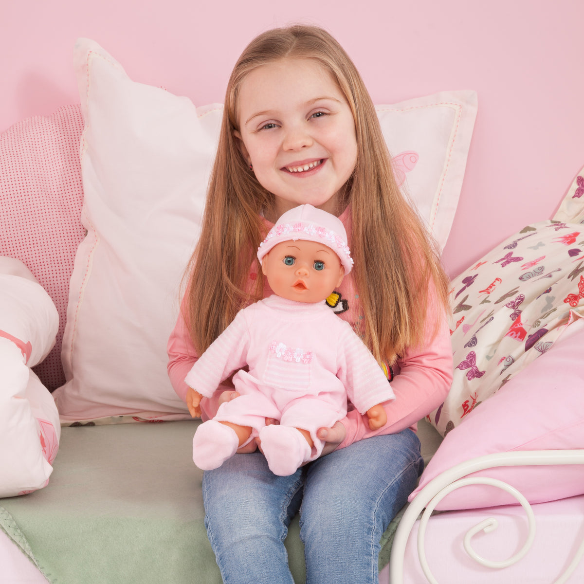 Pink baby doll in frilly hat and white-pink dress with pacifier, held upright.