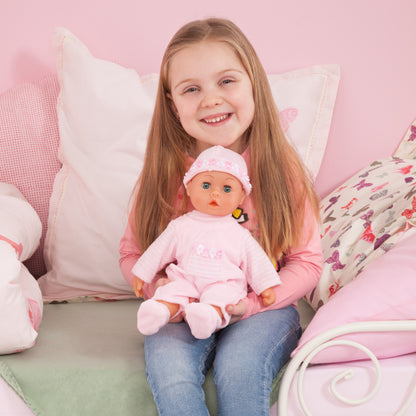 Pink baby doll in frilly hat and white-pink dress with pacifier, held upright.