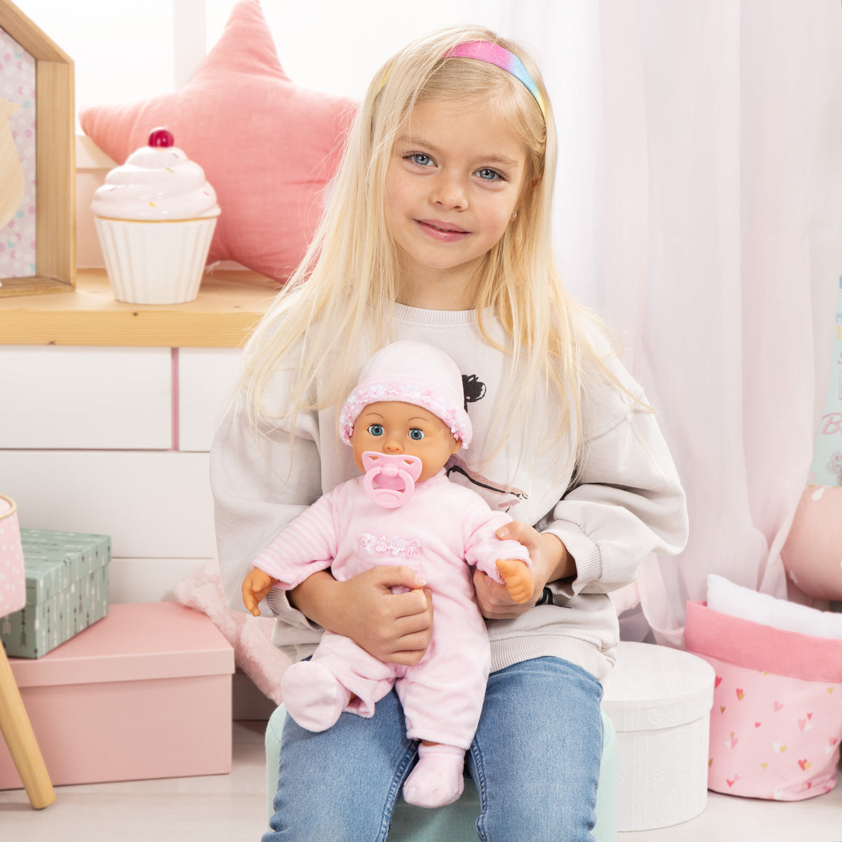Pink baby doll wearing frilly hat and striped dress with pacifier, cradled in arms.