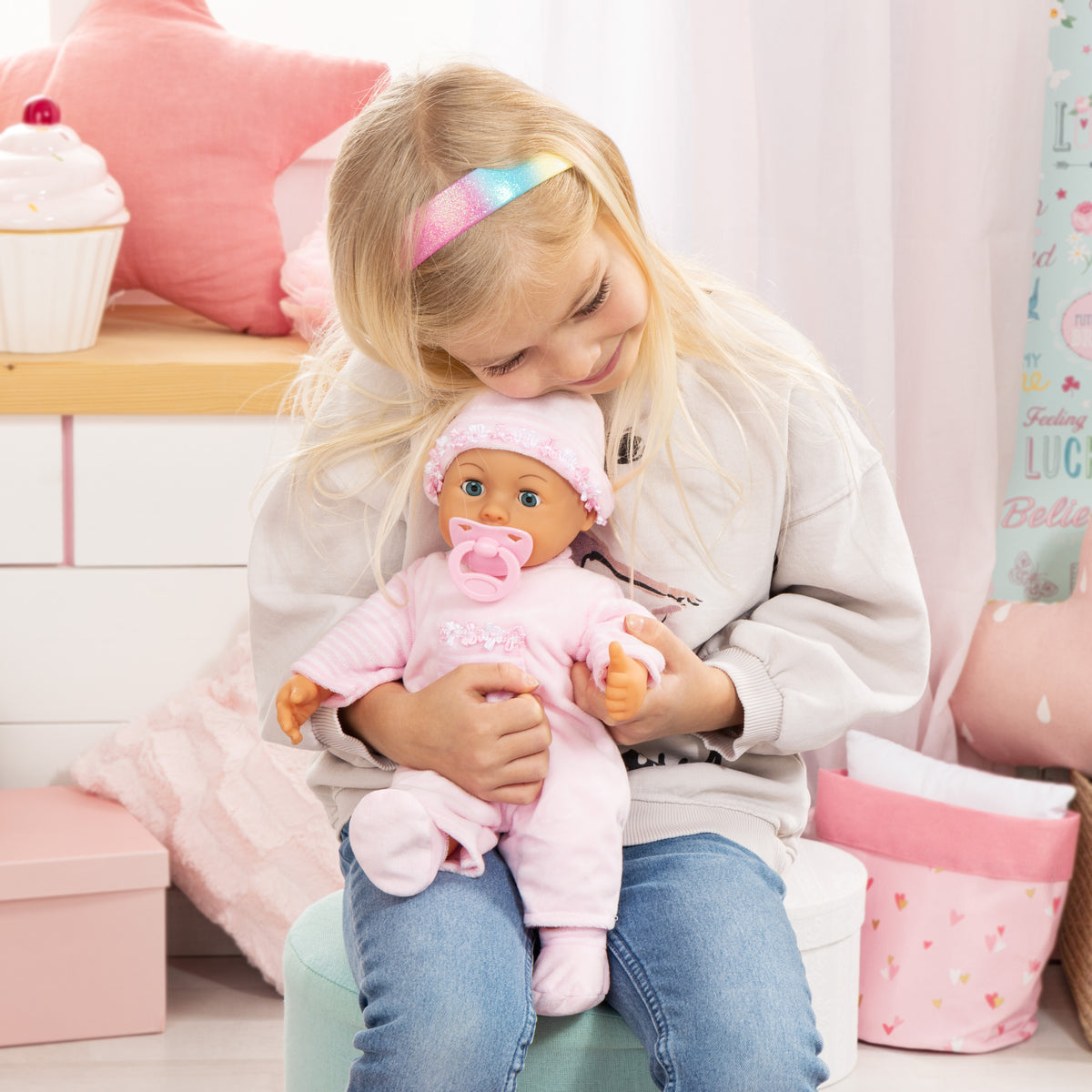 Pink baby doll with frilly hat and pacifier, sitting on lap in pink outfit.