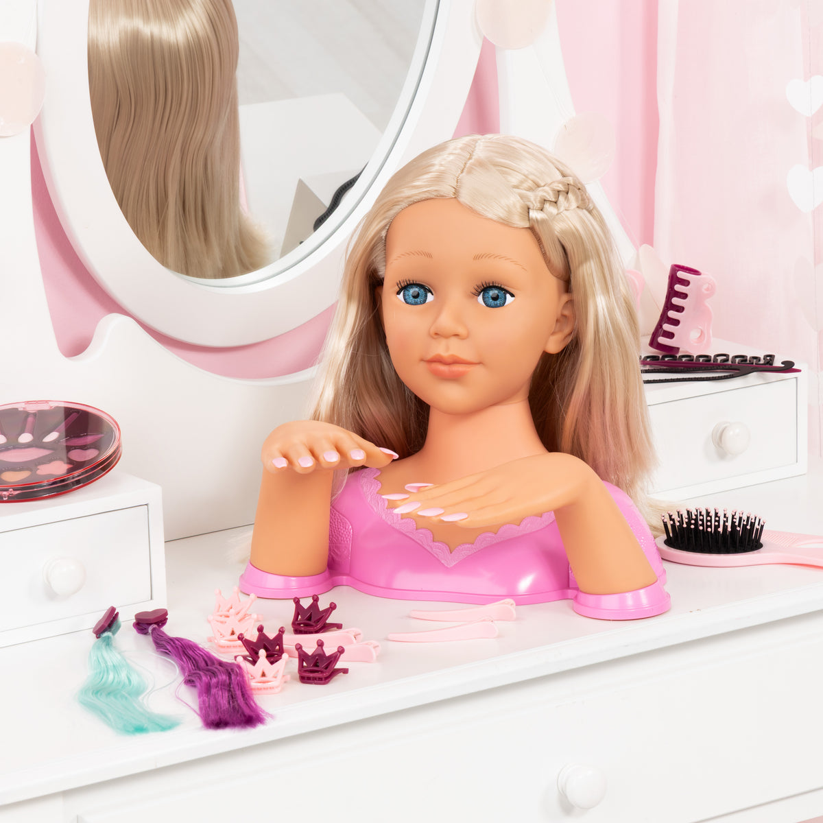 Blonde doll styling head with pink top and glossy nails, posed near hair tools.