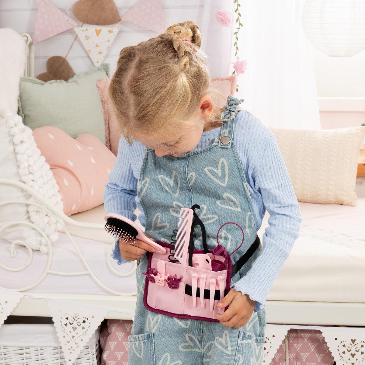 Child holds a pink manicure kit with nail brush and tools near a blonde styling doll