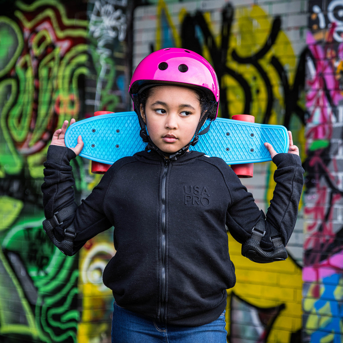 Blue skateboard held behind rider, textured deck and orange wheels visible
