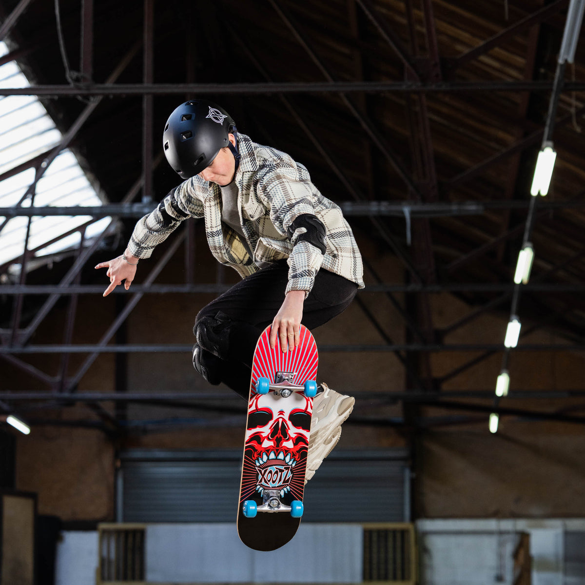 Skull graphic skateboard with blue wheels being ridden at a skatepark