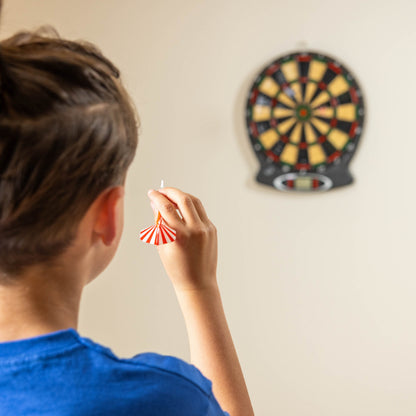 Dartboard on wall with a dart mid-throw held by a person