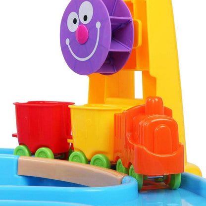 Sand and water table with purple smiling face scoop, orange and red buckets, green wheels