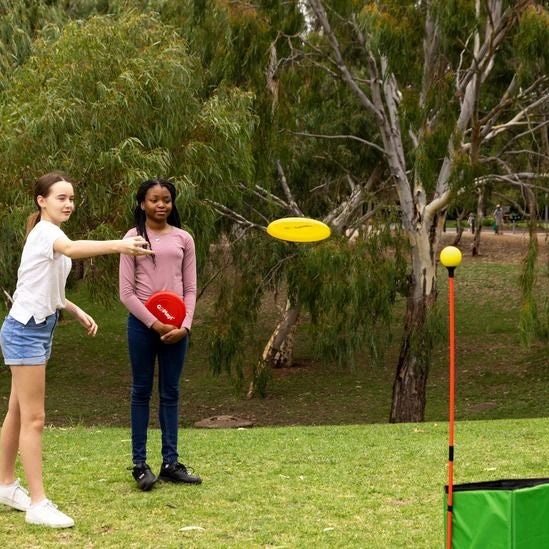 Children playing with a green disc-toss cube and yellow throwing poles in a yard