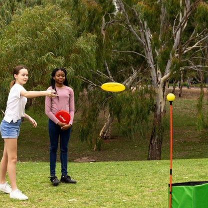 Children playing with a green disc-toss cube and yellow throwing poles in a yard